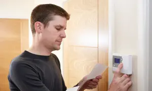 Mężczyzna sprawdza instrukcję, gdzie zamontować czujnik temperatury w domu. Urządzenie jest na ścianie.
