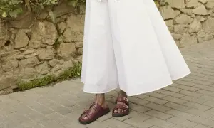 Czerwone sandałki na płaskiej podeszwie idealnie pasują do zwiewnej, białej sukienki. Oto inspiracja, jakie buty do eleganckiej sukienki wybrać na co dzień.
