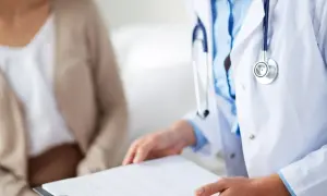 Lekarz w białym kitlu z lh, trzymający dokumenty, rozmawia z pacjentką.