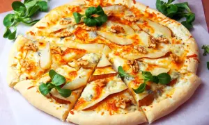 Pyszna pizza z gruszką i serem pleśniowym, posypana orzechami włoskimi i udekorowana świeżą rukolą.