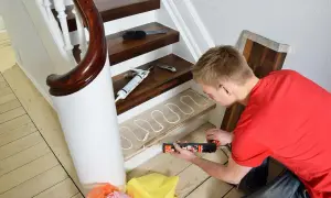 Man renoverar trappa med fogpistol och lim på trappsteg. Nya golvbrädor ligger redo.
