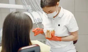 Dentystka w rękawiczkach pokazuje pacjentowi model zęba, wyjaśniając procedurę hemisekcji zęba.