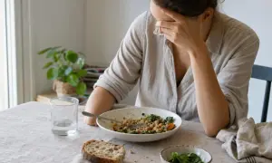 Donna con la mano sulla fronte, sopra un piatto di cibo, soffre di sonnolenza dopo pranzo.