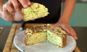 Une main tient une part d'un gâteau aux courgettes, révélant ses fines couches. Ce délice est presque invisible aux courgettes, tant elles sont bien intégrées.