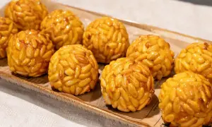 Panellets de boniato cubiertos de piñones dorados, presentados en una bandeja rústica.