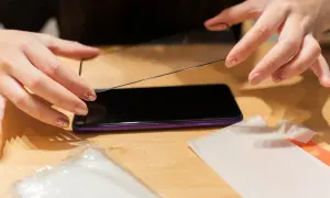 Dłonie przygotowują się do nałożenia szkła hydrożelowego na ekran telefonu.
