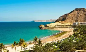 Traumhafte Bucht mit Palmen, Sandstrand und Felsen. Ein Hotel am Hang. Perfekt für Oman Reisetipps.