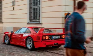Czerwone Ferrari F40 z charakterystycznym spojlerem i okrągłymi światłami mija brukowaną ulicę, a obok przechodzi rozmyta postać mężczyzny.