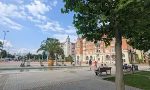 Słoneczny dzień na rynku w Katowicach. Ludzie odpoczywają przy fontannie, a w tle widać zabytkowe kamienice.
