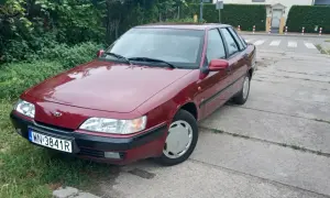 Czerwony Daewoo Espero z tablicą rejestracyjną WN 3841R stoi na betonowej drodze obok zielonego trawnika.