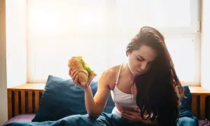 Donna con mal di stomaco tiene un panino, pensando cosa mangiare dopo aver vomitato.