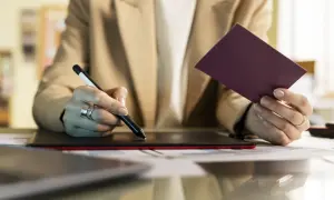 Kobieta z paszportem i piórem cyfrowym na tablecie graficznym, szuka informacji, jak przedłużyć profil zaufany.