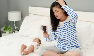 Maman inquiète par la chute de cheveux post-allaitement, cherchant un traitement naturel. Bébé dort paisiblement à côté.