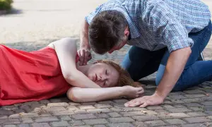 Mężczyzna sprawdza puls u nieprzytomnej kobiety leżącej na boku na chodniku.