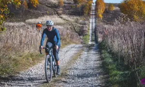 Kobieta na rowerze pokonuje kamienistą ścieżkę w Dolinkach Krakowskich. Jesienne drzewa i trawy tworzą malowniczy krajobraz.
