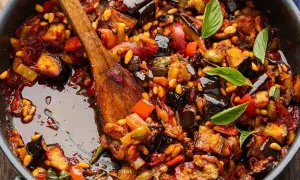 En varm, mustig siciliansk caponata med aubergine, paprika och pinjenötter i en panna, redo att serveras.