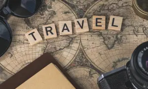 Drewniane klocki z napisem TRAVEL na starej mapie świata, obok okulary, aparat i kompas.