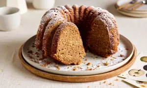 Ein saftiger Kuchen mit Dinkelmehl, bestäubt mit Puderzucker, auf einem Teller mit Holzrand. Ein Stück ist herausgeschnitten.