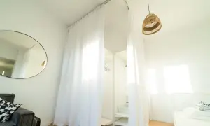 Biała zasłona do szafy zamiast drzwi, tworzy przytulną przestrzeń. W tle widać półki i wieszaki.