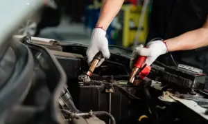 Manos enguantadas conectando cables a la batería de un coche. Es hora de desconectar la batería del coche para un mantenimiento seguro.