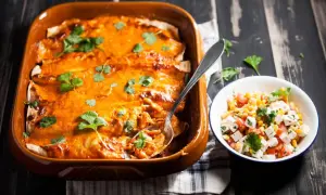 Enchiladas kyckling i en ugnsform, toppade med ost och koriander, bredvid en skål med majs- och tomatsallad.