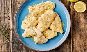 Piatto di pollo al limone su un piatto blu, con limone e rosmarino sullo sfondo.