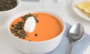 En skål med krämig linssoppa med potatis, toppad med en klick gräddfil och pumpafrön. En sked ligger bredvid.