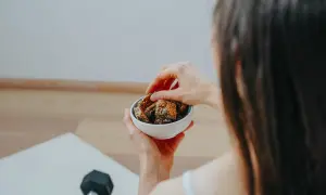 Frau isst vor oder nach dem Sport einen gesunden Snack aus einer Schüssel mit Nüssen und Trockenfrüchten.
