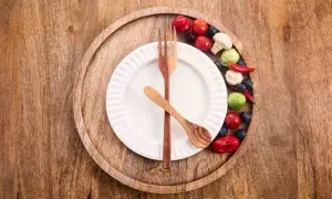Ein leeres Teller mit Holzbesteck und bunte Gemüse-Beeren-Deko. Bereit für 36 Stunden Fasten.