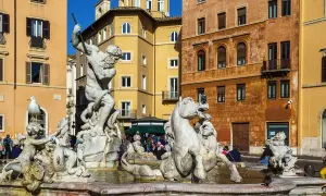 La Fuente de Neptuno en Roma, con su imponente estatua de mármol luchando contra un pulpo, rodeada de caballos marinos y figuras mitológicas, bajo el sol y edificios coloridos.