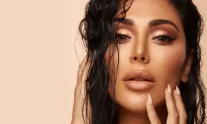 Un visage de femme au maquillage sophistiqué, avec des yeux cuivrés et des lèvres en teinte nude. Ses cheveux mouillés encadrent son visage.