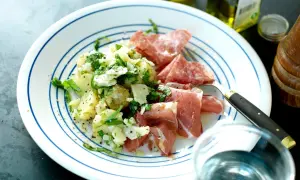 En tallrik med potatissallad med parmesan, serverad med salami och prosciutto. En utsökt måltid!