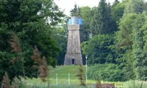 Kamienna wieża Bismarcka w Szczecinku, otoczona zielenią, z błękitnym elementem na szczycie.