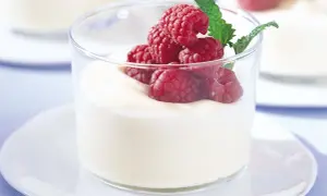 En len vit chokladmousse toppas med färska hallon och en myntakvist i ett glas.