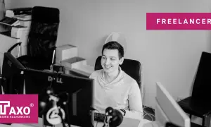 Uśmiechnięty freelancer przy biurku z komputerami. Czy freelancer musi mieć działalność gospodarczą? Zapytaj TAXO.