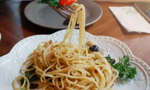 Widok z bliska na talerz pysznego spaghetti aglio olio, z widelcem unoszącym porcję makaronu, listkami bazylii i pomidorkiem.