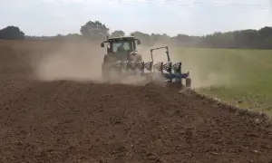 Traktor z pługiem orze pole, wzbijając tumany kurzu. To przygotowanie gleby do kolejnego sezonu, być może z myślą o wapnowaniu gleby.