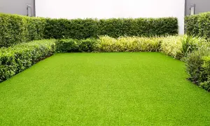 Un jardín impecable con césped artificial verde vibrante, rodeado de setos y plantas. Ideal para quienes buscan cual es el mejor césped artificial para jardín.