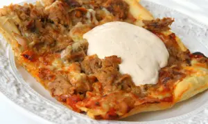 En bit pizza med tonfisk och fetaost, toppad med en krämig sås.