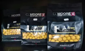 Trzy opakowania kulek proteinowych CC Moore Live System w różnych rozmiarach. Kulki są żółte, widoczne przez przezroczyste okienko.
