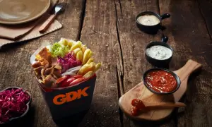 Kebab w pudełku z frytkami, warzywami i sosami na drewnianym stole.