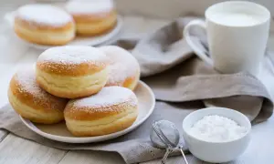 Un mucchio di soffici bomboloni alla crema, spolverati di zucchero a velo, pronti per essere gustati con una tazza di latte.