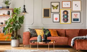 Oryginalna aranżacja ściany w salonie z pomarańczową kanapą, roślinami i galerią obrazów.
