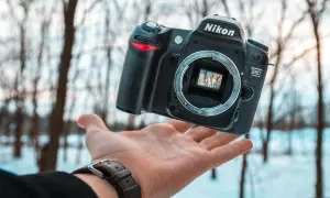 Oto jak wygląda aparat fotograficzny Nikon D80, unoszący się nad dłonią na tle zimowego lasu.