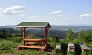 Drewniana wiata z ławkami i stołem na tle malowniczego krajobrazu Dolnego Śląska. Idealne miejsce na odpoczynek podczas zwiedzania wież widokowych.