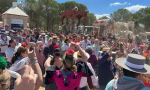 Multitud celebra con alegría, bailando y cantando al paso de una carreta adornada. Se percibe el espíritu de una sevillana rociera en pleno fervor.