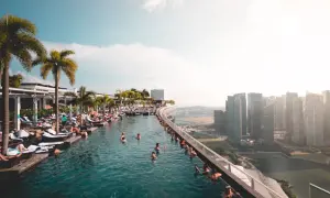 Menschen entspannen sich in einem Infinity-Pool mit Blick auf die Skyline von Singapur. Die **Singapur Regeln** für den Pool sind klar: Genießen!