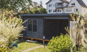 Modernes Gartenhaus mit Doppeltür und überdachter Veranda, ideal als Teil einer bauanleitung gartenhaus. Umgeben von üppigem Grün.