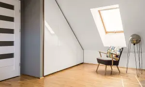 Nowoczesne drzwi na poddasze prowadzą do pokoju ze skosami. Wnętrze zdobi fotel w komiksowym stylu i białe szafy wnękowe.