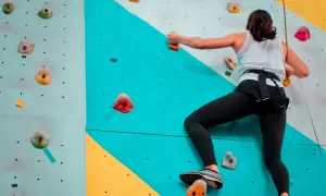 Une femme en tenue de sport fait de l'escalade sur un mur coloré, cherchant la prochaine prise.